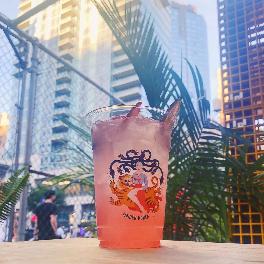 A pink cocktail in a Maiden Korea cup among the palms