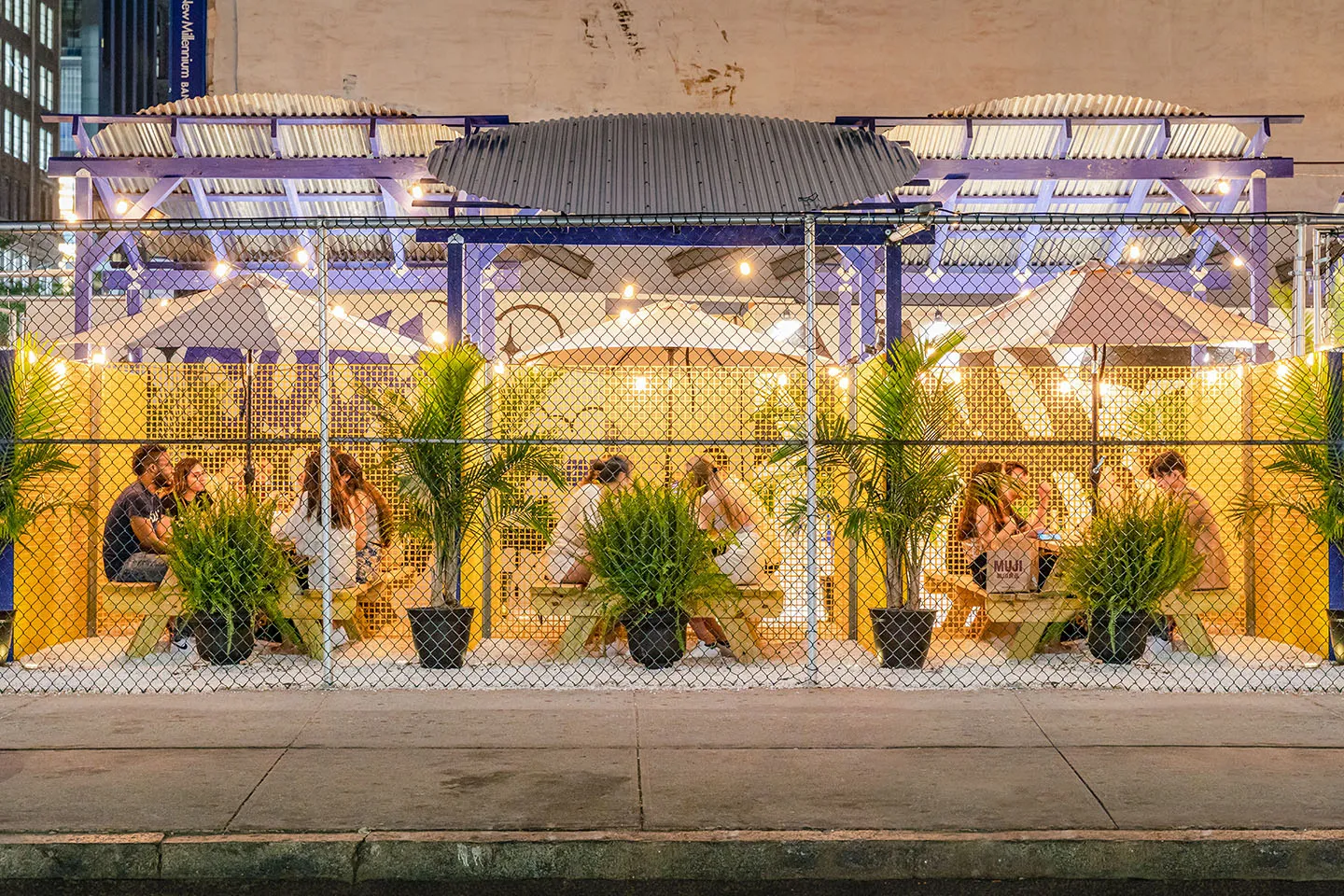 Dining booths behind the fence at Maiden Korea, lit up at dusk