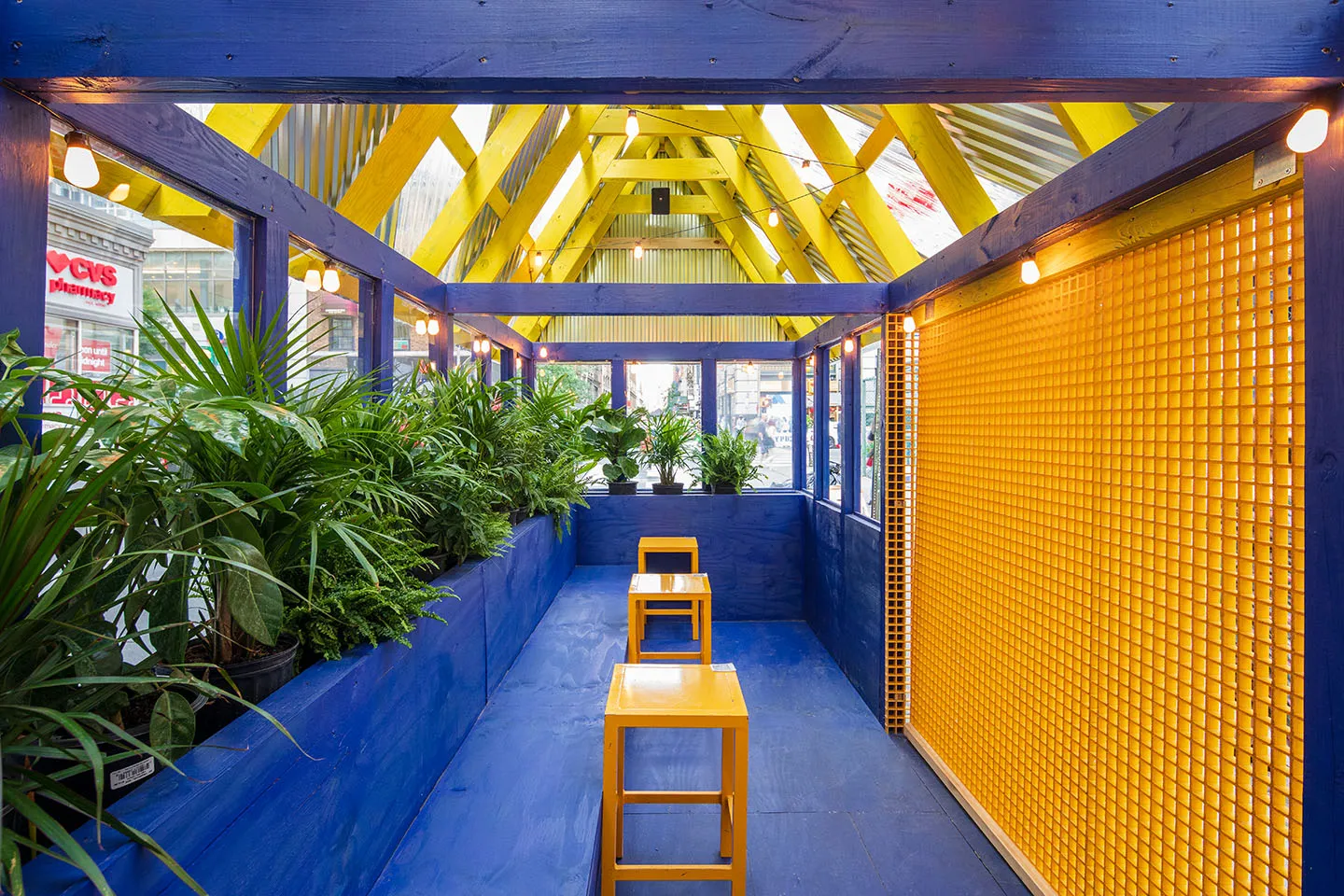 Inside a cobalt-blue booth with yellow mesh walls and planters
